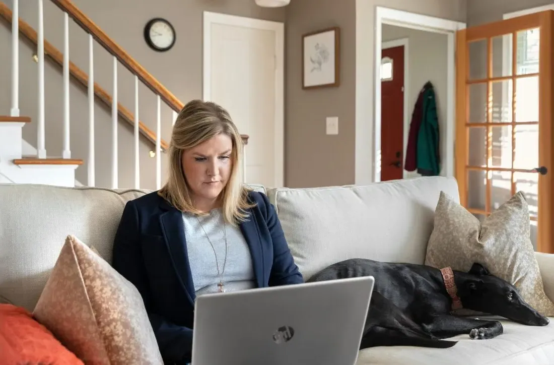 Student learning online from couch, with dog laying beside them.